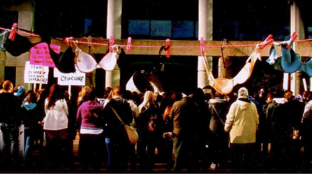 Groupe manifestant devant une corde où sont suspendues des soutiens-gorge